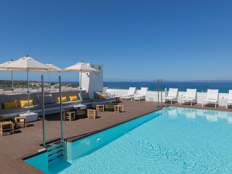 Panoramiczny widok na basen z białymi leżakami i parasolami pod jasnym, niebieskim niebem.