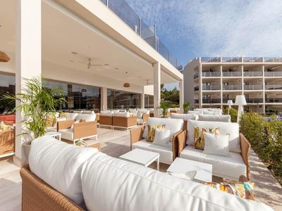 Grande terrasse avec mobilier de lounge blanc moderne devant un bâtiment hôtelier par temps ensoleillé.