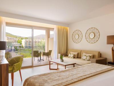 Chambre d'hôtel lumineuse avec lit double, coin salon et balcon donnant sur la piscine et le jardin.