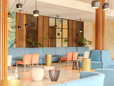 Hall d'hôtel lumineux avec bancs bleus, chaises orange et lampes suspendues.