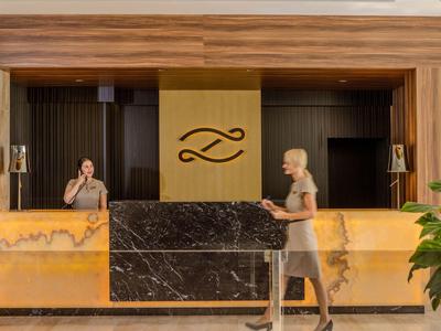 Réception d'hôtel avec comptoir en marbre élégant et deux employés, une au téléphone, une marchant.