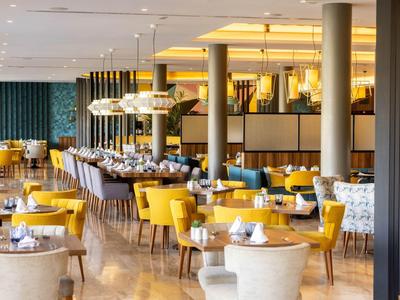 Salle à manger moderne d'hôtel avec chaises jaunes et grises et éclairage élégant.