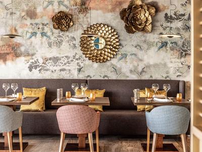 Elegant restaurant met kleurrijke stoelen, bruine bank en decoratieve wandkunst.