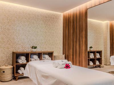 Salle de soin avec table de massage, tapis, meubles en bois et éclairage doux.