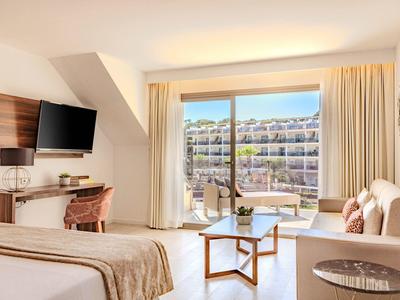 Chambre d'hôtel lumineuse avec lit, canapé, télévision et balcon donnant sur la piscine.
