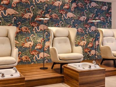 Trois fauteuils de pédicure confortables devant un mur coloré à motif flamant rose dans un spa.