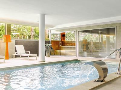 Piscine intérieure moderne avec fontaine d'eau, chaises longues et grandes fenêtres donnant sur le jardin.
