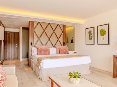 Chambre d'hôtel lumineuse avec lit double, coussins décoratifs et tableaux de plantes encadrés au mur.