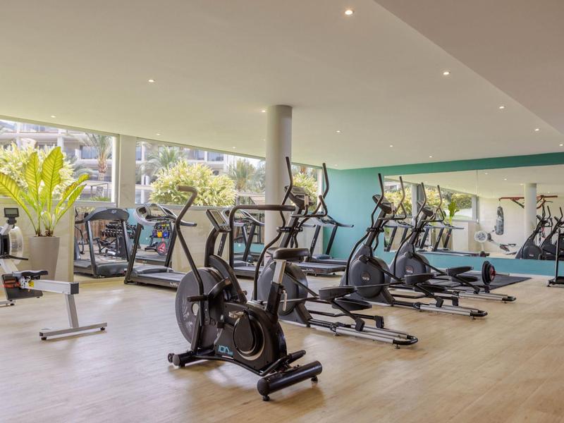 Salle de sport moderne avec des elliptique et de grandes fenêtres laissant entrer la lumière naturelle.