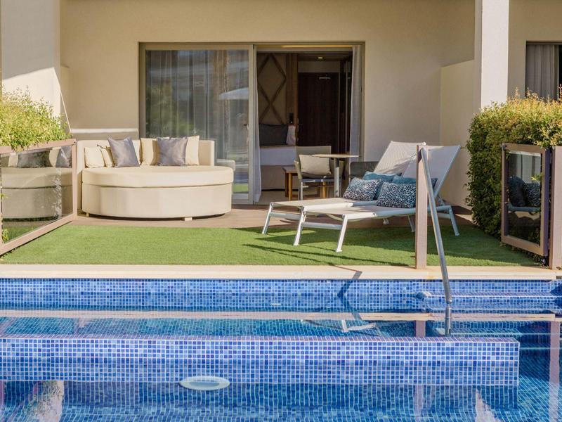 Espace hôtelier relaxant avec canapé, chaise et piscine devant une terrasse avec portes.