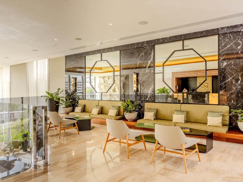 Hall d'hôtel lumineux avec sièges modernes, grands miroirs et murs en marbre.