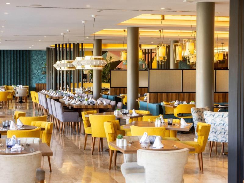 Salle à manger moderne d'hôtel avec chaises jaunes et grises et éclairage élégant.