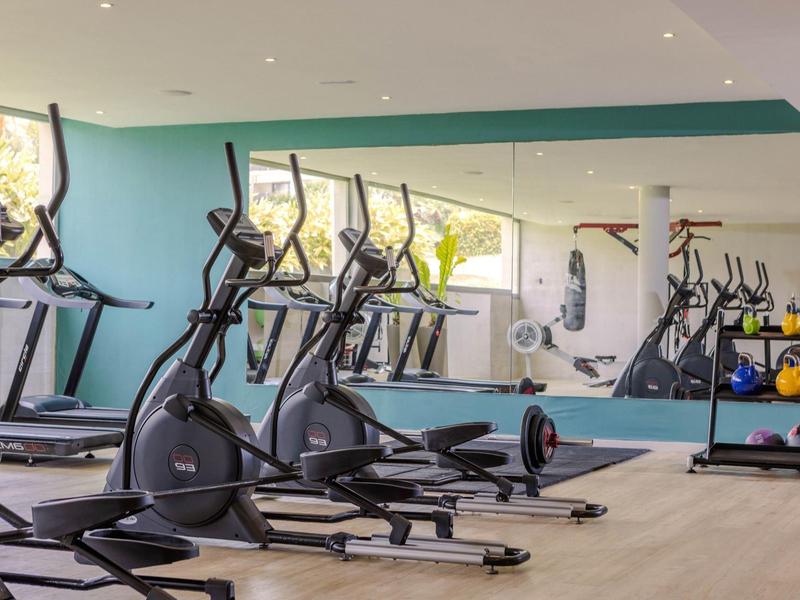 Équipements de fitness modernes et haltères dans une salle de sport lumineuse et bien équipée avec un mur miroir.