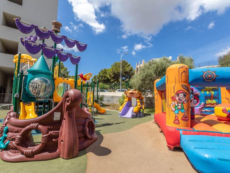 Aire de jeux colorée avec structures d'escalade et château gonflable sous ciel bleu à côté de l'hôtel.