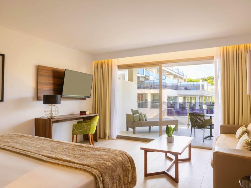 Chambre d'hôtel moderne avec lit, bureau, télévision et balcon donnant sur l'extérieur.