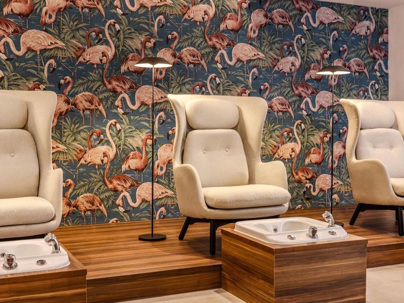 Trois fauteuils de pédicure confortables devant un mur coloré à motif flamant rose dans un spa.
