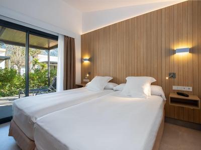 Modern ingerichte hotelkamer met twee eenpersoonsbedden en uitzicht op tuin door grote ramen.