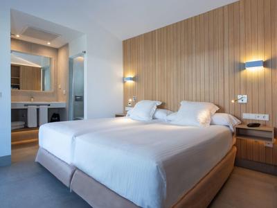 Modern hotelkamer met tweepersoonsbed, houten wand en badkamer op de achtergrond.