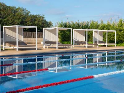 Helder zwembad met rode banen en moderne witte ligbedden op de achtergrond.