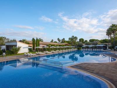 Groot hotelzwembad met ligstoelen en palmbomen onder een heldere lucht.