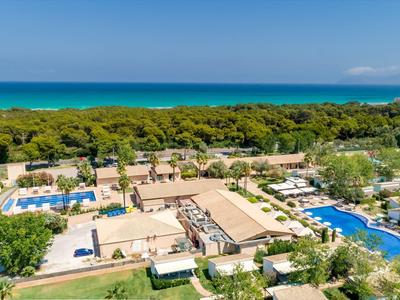 Luchtfoto van een resort met meerdere zwembaden, parasols en weelderig groen aan zee.