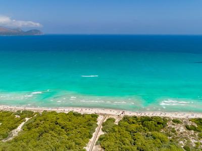 Strand met groene struiken, turkoois water en blauwe lucht met een wolk.