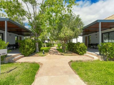 Pad tussen moderne bungalows met groene struiken en bomen onder een blauwe lucht.
