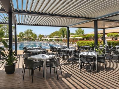 Buiten eetgedeelte met tafels en stoelen naast een zwembad onder een pergola.