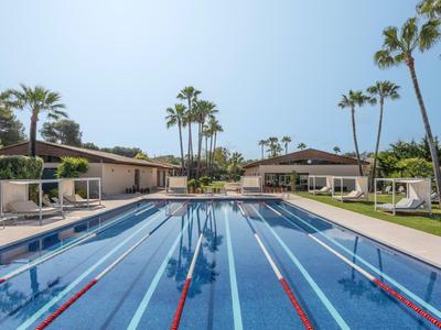 Buiten zwembad met banen omgeven door palmbomen en ligstoelen bij helder weer.