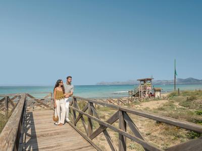 Koppel wandelt over houten vlonder langs zandstrand en oceaan onder heldere lucht.