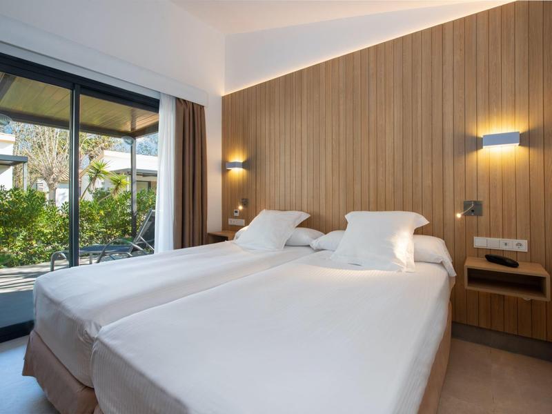 Modern ingerichte hotelkamer met twee eenpersoonsbedden en uitzicht op tuin door grote ramen.