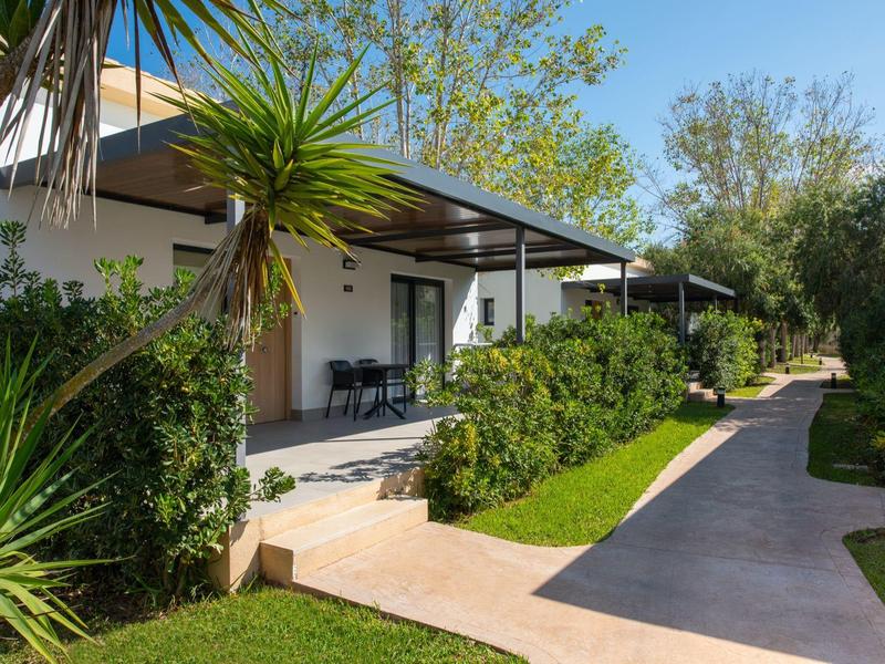 Moderne hotelbungalows met terrassen in een groene, zonnige tuin.