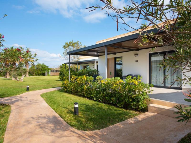 Modern vakantiehuis met veranda en tuin, omgeven door groen landschap en blauwe lucht.
