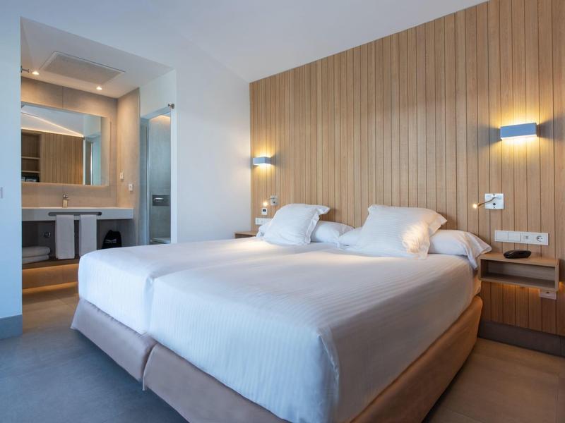 Modern hotelkamer met tweepersoonsbed, houten wand en badkamer op de achtergrond.