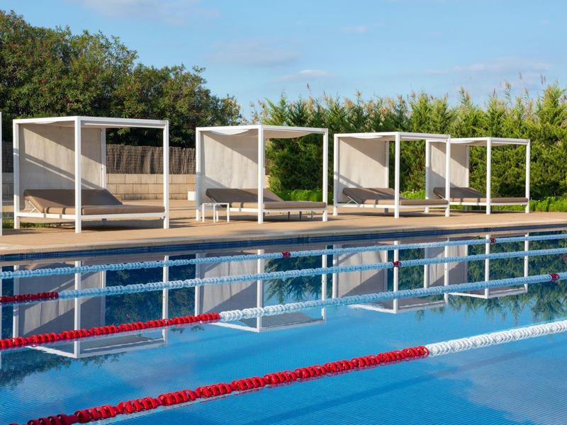 Helder zwembad met rode banen en moderne witte ligbedden op de achtergrond.