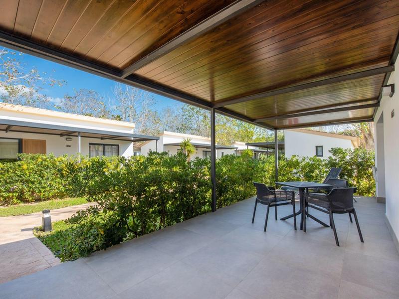 Overdekt terras met stoelen en tafel naast een groene tuin in een vakantiepark.