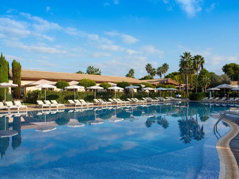 Groot zwembad met ligstoelen en parasols in een hotelresort bij blauwe lucht.
