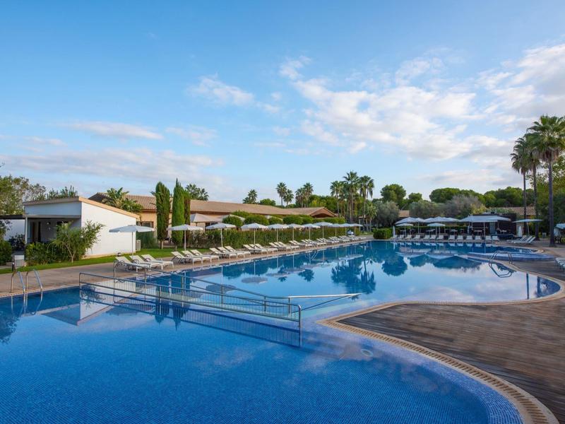 Groot hotelzwembad met ligstoelen en palmbomen onder een heldere lucht.