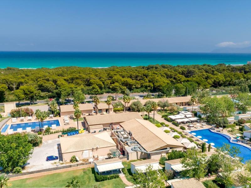 Luchtfoto van een resort met meerdere zwembaden, parasols en weelderig groen aan zee.