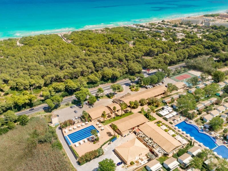 Luchtfoto van een resort met zwembaden, omgeven door bos en strand.