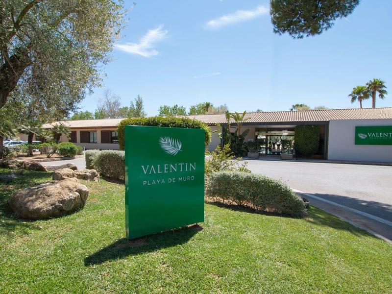 Hotel onder zonnige hemel met groen gras en groen bord bij ingang.