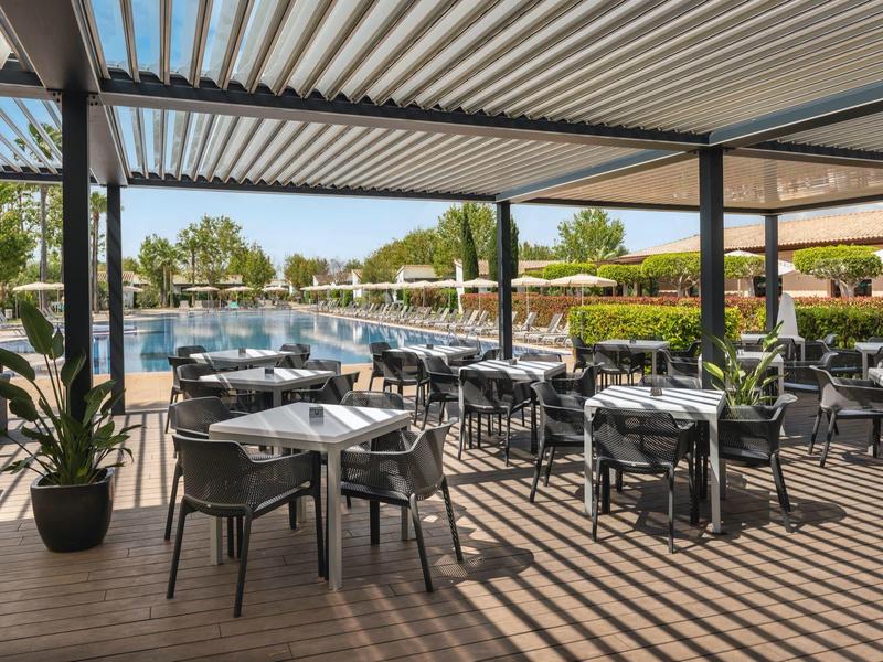 Buiten eetgedeelte met tafels en stoelen naast een zwembad onder een pergola.