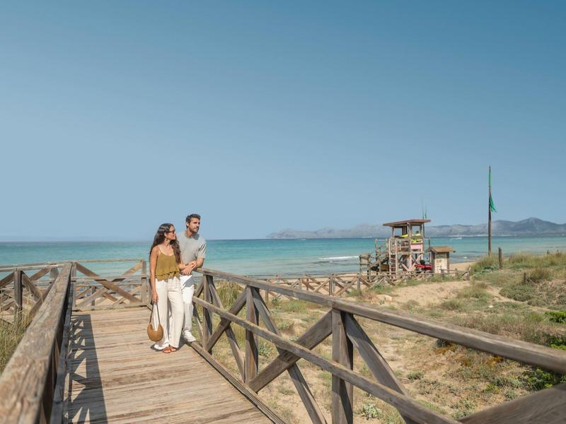 Koppel wandelt over houten vlonder langs zandstrand en oceaan onder heldere lucht.