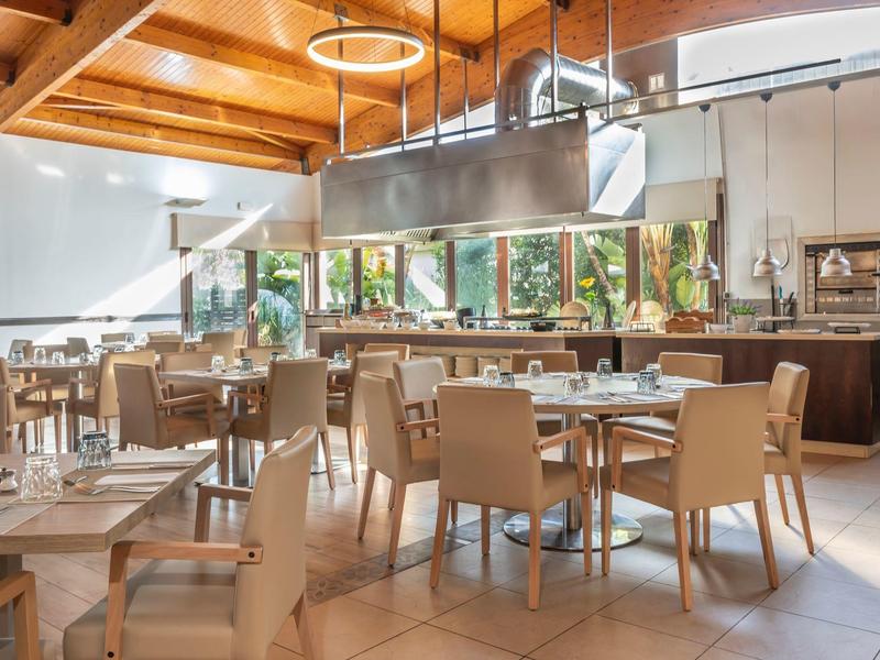Licht hotelrestaurant met houten plafond, beige stoelen en tafels gedekt voor diner.