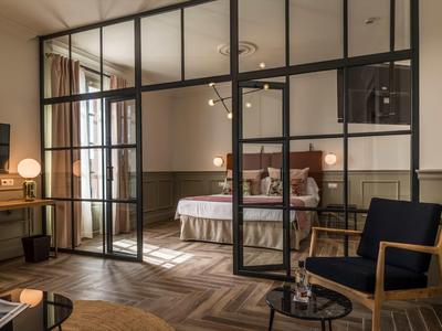 Modern hotelkamer met glazen wand, gezellig bed en zithoek met stoel en tafel.