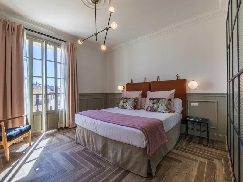 Gezellige hotelkamer met tweepersoonsbed, zithoek en balkon bij daglicht.