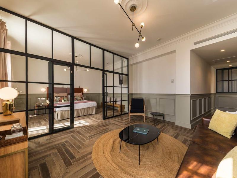 Modern hotelkamer met gezellige zithoek en aparte slaapkamer achter glazen wand.