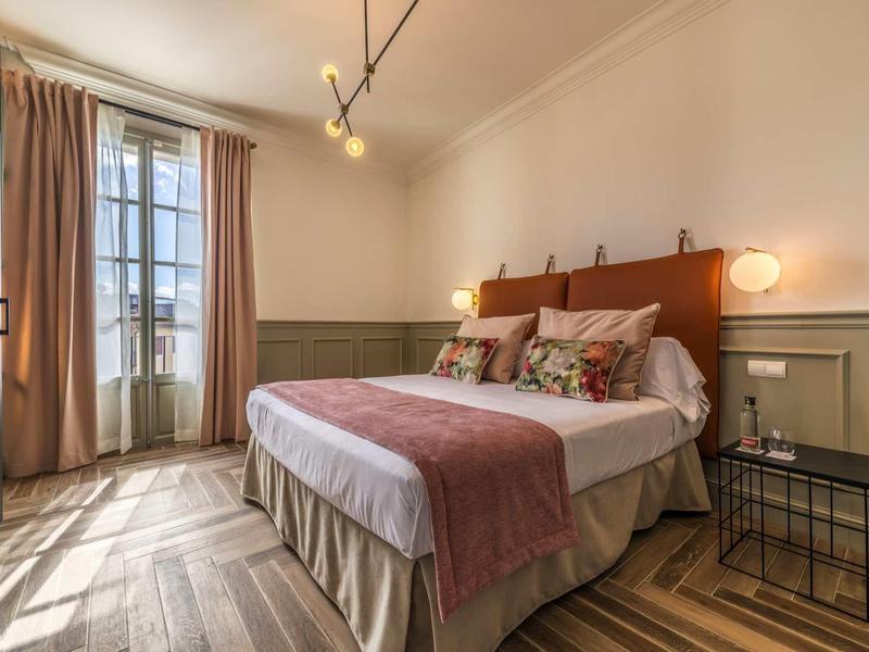 Gezellige hotelkamer met groot bed, decoratieve kussens en daglicht door hoge ramen.