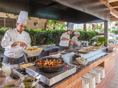 Tři kuchaři připravují čerstvě uvařená jídla v venkovní kuchyni hotelu.