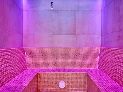 Prázdná parní místnost s růžovými dlaždicemi a fialovým osvětlením.